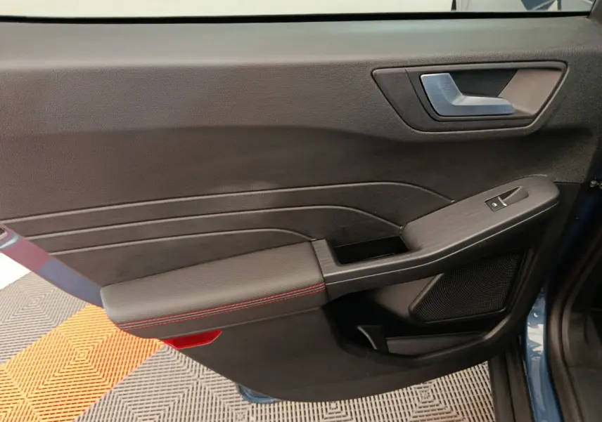 Gros plan sur la porte intérieure côté gauche du Ford Kuga bleu, avec surpiqûres rouges et commande de vitre.
