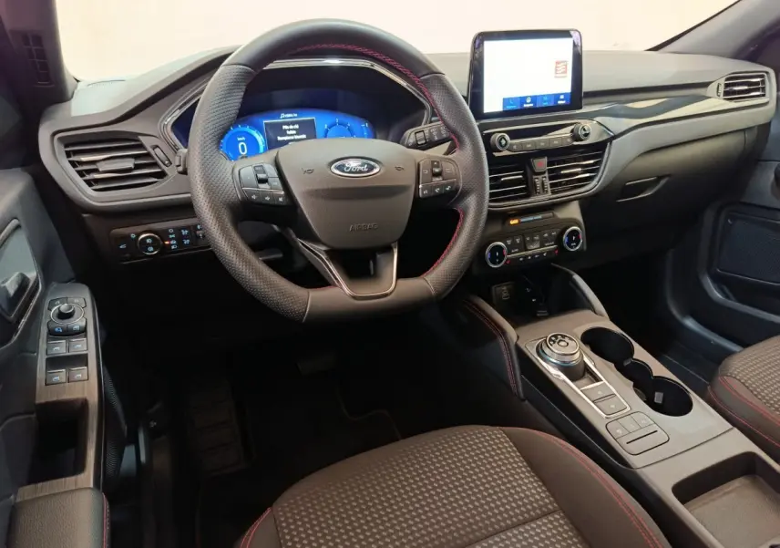 Intérieur du Ford Kuga 2024 vue côté conducteur, tableau de bord noir avec écran tactile et volant cuir noir.