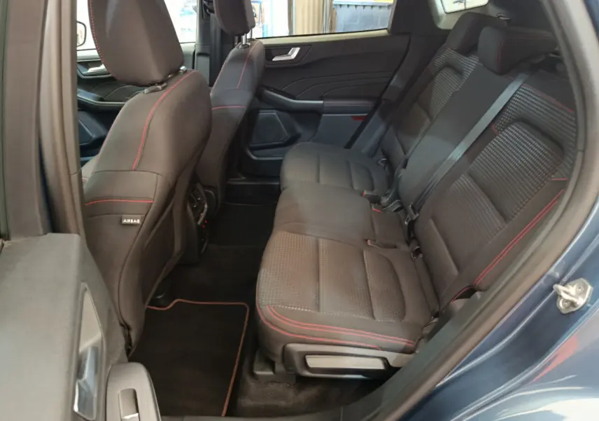 Vue côté droit sur l’intérieur arrière du Ford Kuga bleu 2024, sièges noirs avec surpiqûres rouges et ceintures grises.