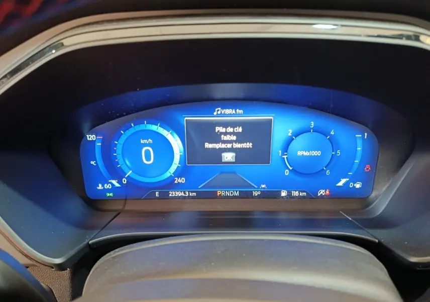 Tableau de bord numérique bleu du Ford Kuga 2024 affichant vitesse, régime et message clé faible.