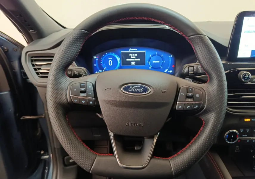 Volant en cuir noir avec surpiqûres rouges du Ford Kuga 2024, tableau de bord numérique bleu en arrière-plan.