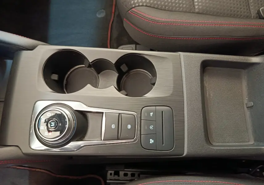 Vue plongeante sur la console centrale noire du Ford Kuga bleu 2024 avec molette de boîte auto et surpiqûres rouges.