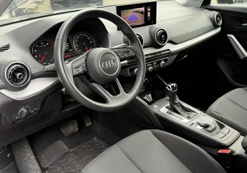 Intérieur de l'Audi Q2 2023 vu côté conducteur, tableau de bord noir avec écran caméra de recul et console centrale moderne.