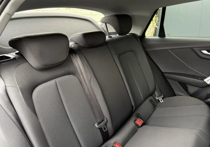 Vue intérieure sur la banquette arrière noire de l'Audi Q2 35 TFSI S-Line, avec appuie-têtes et ceintures visibles.