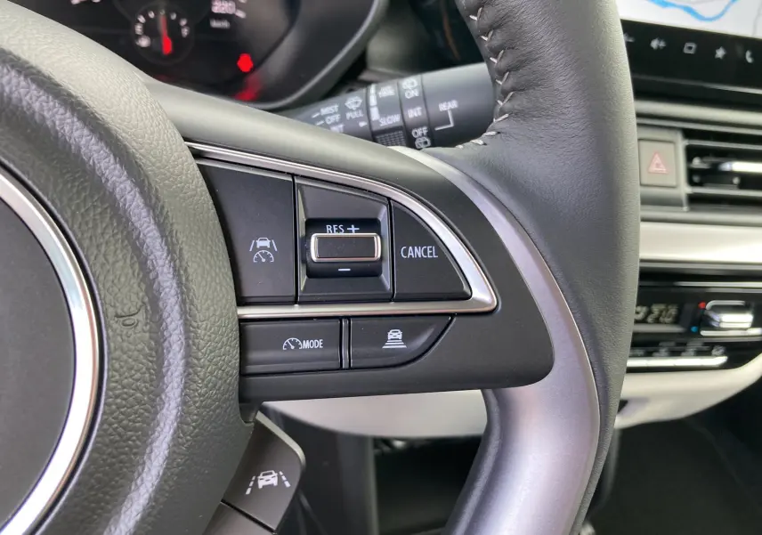 Gros plan sur le volant cuir multifonctions de la Suzuki Swift 2025, avec commandes de régulateur de vitesse visibles.