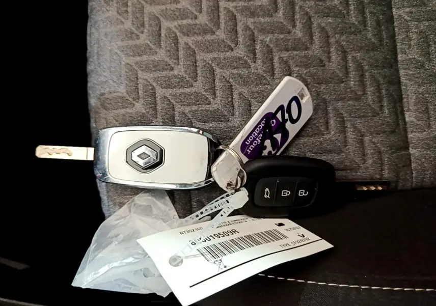 Clé Renault grise et noire posée sur un siège tissu gris à motif chevrons, avec porte-clés et étiquette.