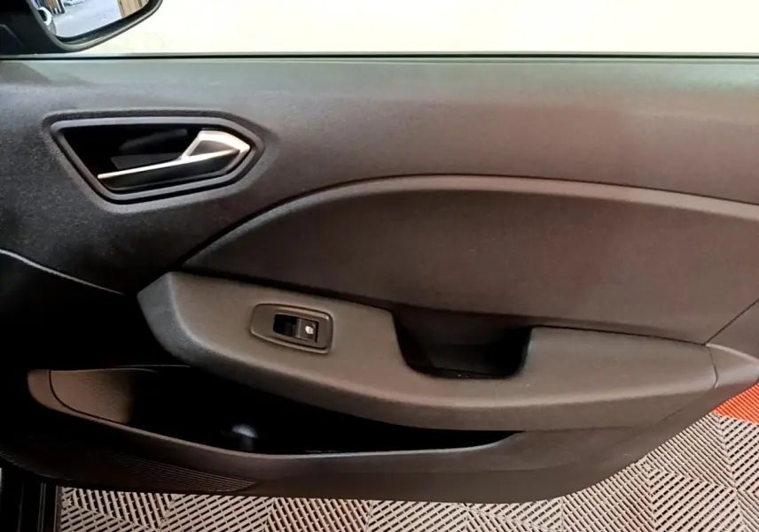 Vue intérieure du panneau de porte côté conducteur de la Renault Clio gris foncé avec poignée argentée et commande de fenêtre électrique.