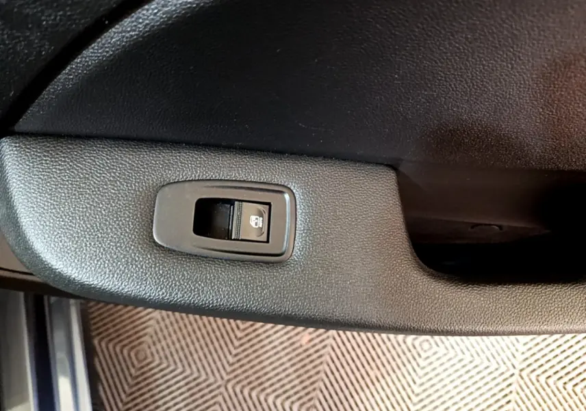 Gros plan sur le bouton de verrouillage centralisé dans la portière intérieure noire d’une Renault Clio gris foncé.