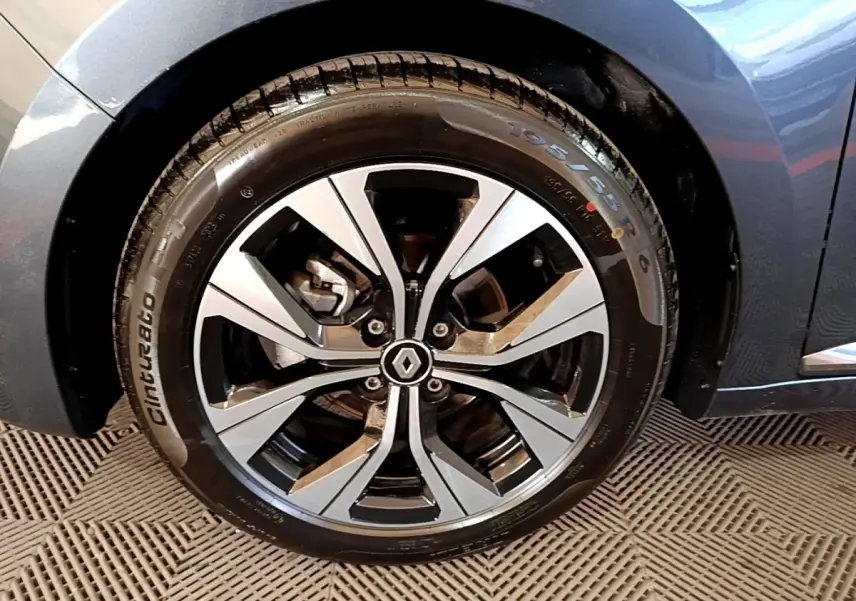 Gros plan sur la roue avant droite d'une Renault Clio gris foncé, avec jante alliage au design moderne et logo central Renault.