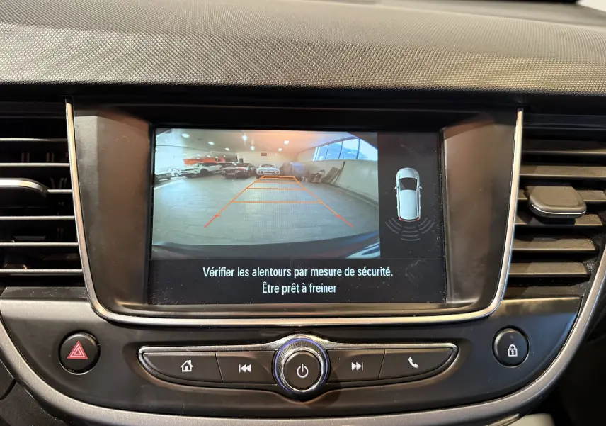 Vue de l'écran central montrant la caméra de recul de l'Opel Crossland rouge, avec les lignes de guidage et l'alerte de sécurité.