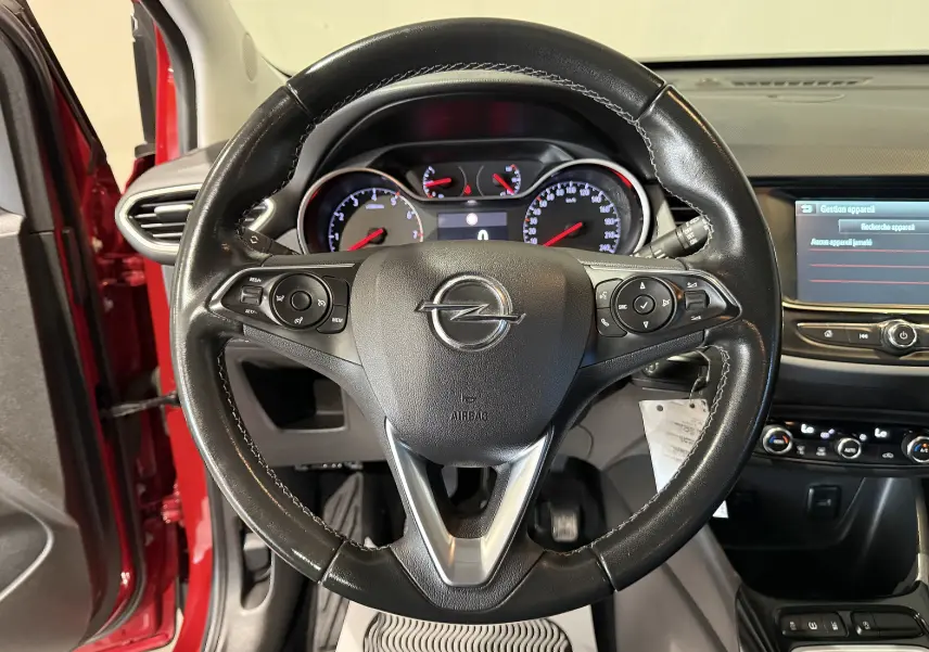 Vue intérieure centrée sur le volant noir de l’Opel Crossland rouge, avec tableau de bord et écran multimédia visibles.