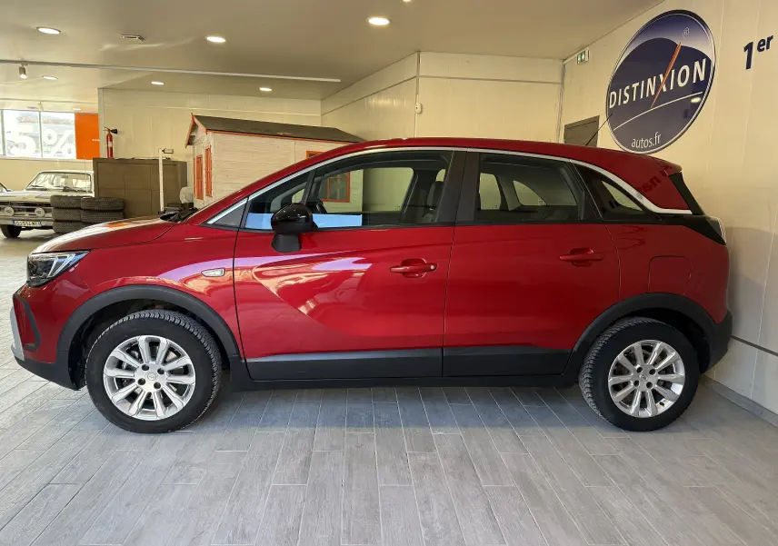 Vue de profil côté gauche d’un Opel Crossland rouge 2022 dans un showroom avec jantes argentées et rétroviseurs noirs.