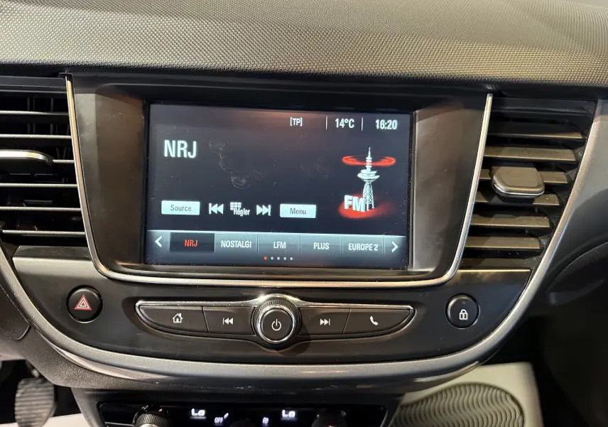 Gros plan sur l’écran multimédia central de l’Opel Crossland 2022 affichant la radio NRJ, entouré de commandes et grilles d’aération noires.