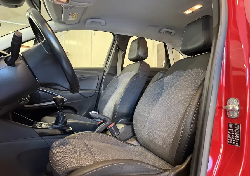 Vue intérieure côté gauche de l’Opel Crossland rouge 2022, montrant les sièges avant en tissu et la boîte manuelle.