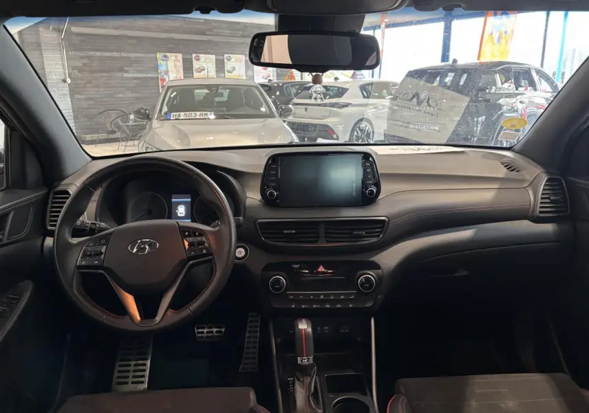 Vue intérieure avant du Hyundai Tucson noir 2020, tableau de bord et volant sport N Line avec surpiqûres rouges.