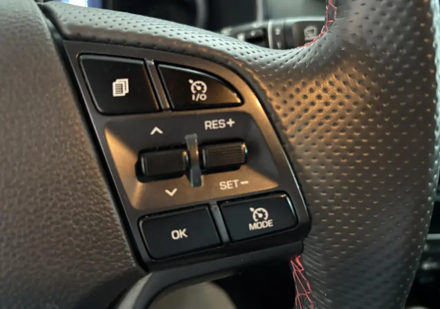 Gros plan sur les commandes de régulateur de vitesse du volant cuir noir perforé avec surpiqûres rouges du Hyundai Tucson N Line.