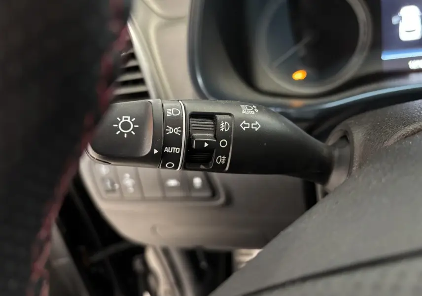Gros plan sur la manette de commande des feux et clignotants du Hyundai Tucson noir, intérieur avec volant perforé.