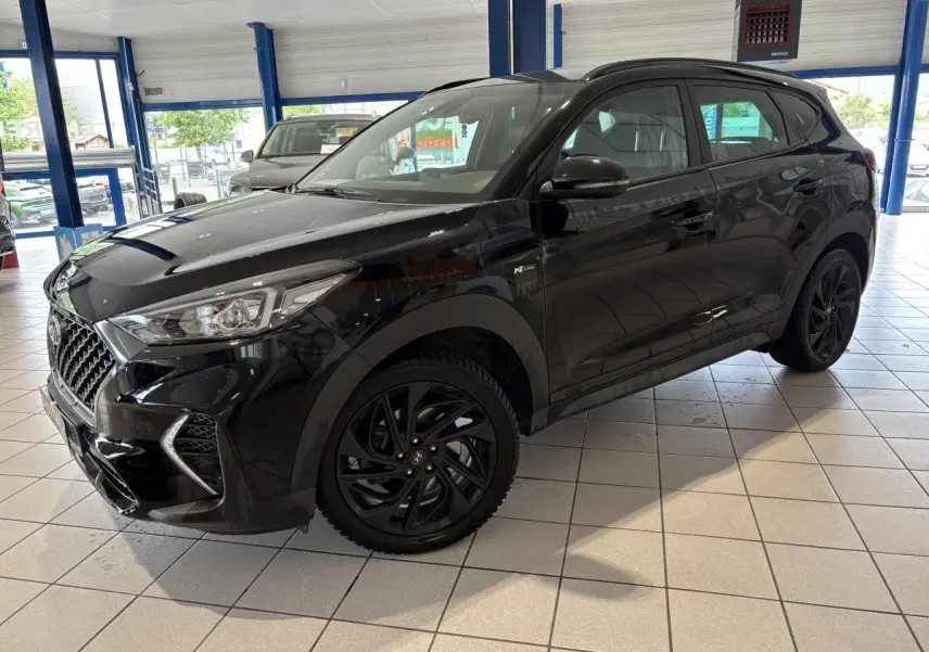Hyundai Tucson noir en 3/4 avant droit, avec jantes alliage noires et badge N Line visible sur l'aile avant.