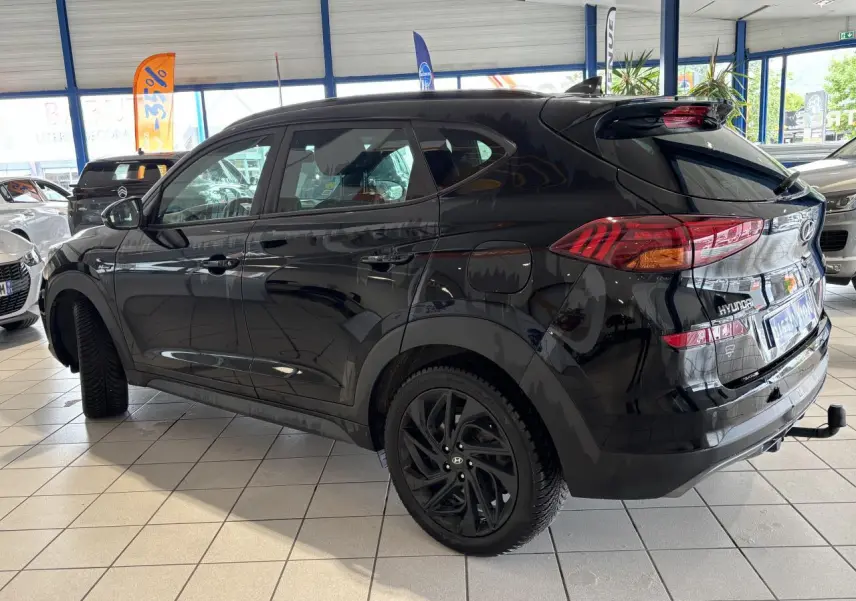 Vue 3/4 arrière gauche du Hyundai Tucson noir métallisé avec jantes alliage noires et attelage en concession.