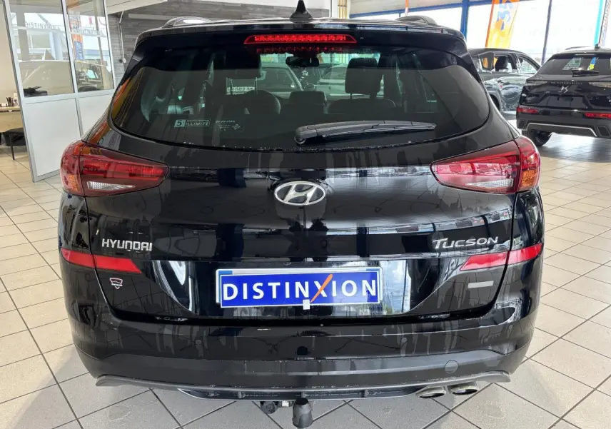 Vue arrière d'un Hyundai Tucson noir métallisé avec double sortie d'échappement et logo distinctif en concession.