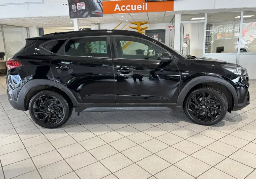 Vue latérale droite d'un Hyundai Tucson noir métallisé N Line avec jantes alliage noires en showroom.