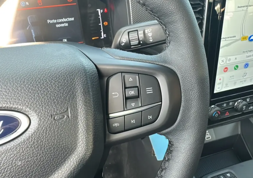 Gros plan sur le volant cuir noir du Ford Ranger 2026 avec commandes multifonctions et écran tactile de navigation visible.