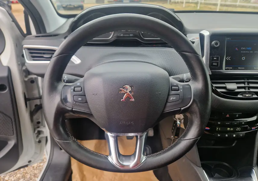 Vue intérieure centrée sur le volant noir de la Peugeot 208 blanc nacré, avec tableau de bord et écran tactile visibles.