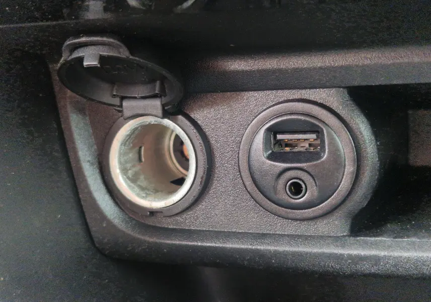 Prise allume-cigare ouverte et port USB avec entrée auxiliaire sur la console centrale d'une Peugeot 208 blanche nacrée.
