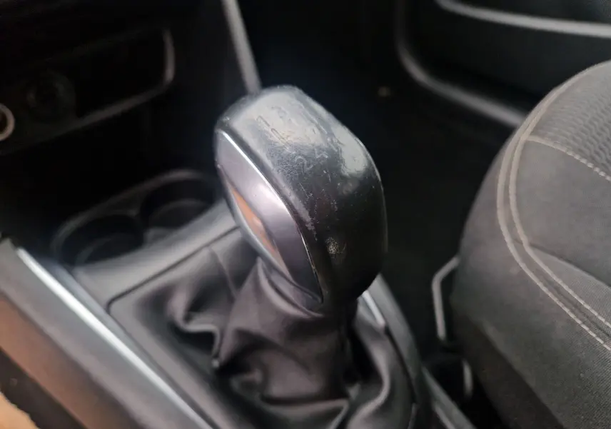 Gros plan sur le levier de vitesses manuel noir de la Peugeot 208 blanc nacré, avec siège tissu gris à droite.