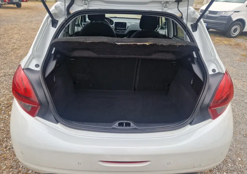 Coffre ouvert vu de l’arrière d’une Peugeot 208 blanc nacré, intérieur noir et banquette arrière visible.