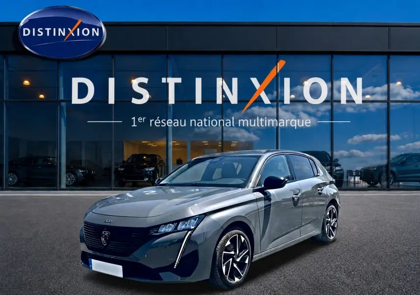 Peugeot 308 gris vue 3/4 avant droit, avec phares LED et jantes alliage distinctives, devant showroom Distinxion.