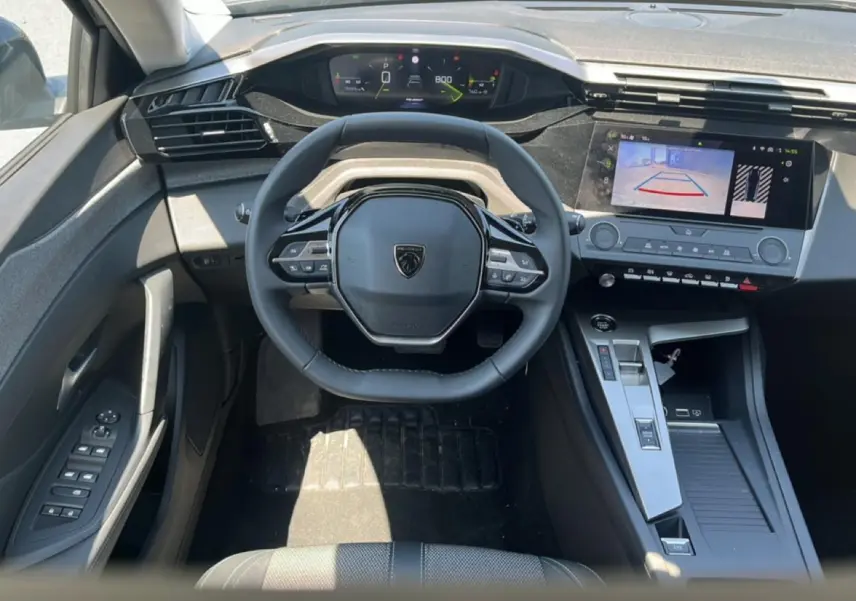 Vue intérieure frontale du poste de conduite de la Peugeot 308 gris, avec volant multifonction et écran tactile affichant la caméra de recul.