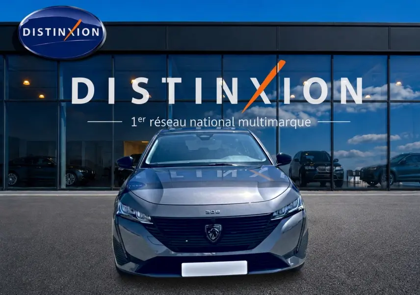 Peugeot 308 gris vue de face, avec calandre noire et logo lion distinctif, devant une vitrine Distinxion.