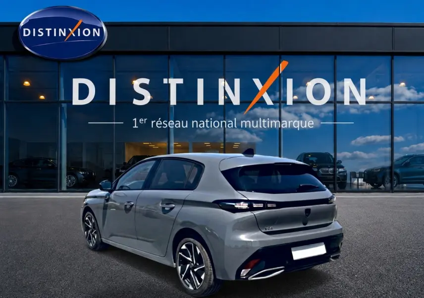 Peugeot 308 gris en 3/4 arrière droit, avec feux arrière LED et jantes alliage, devant une vitrine Distinxion.