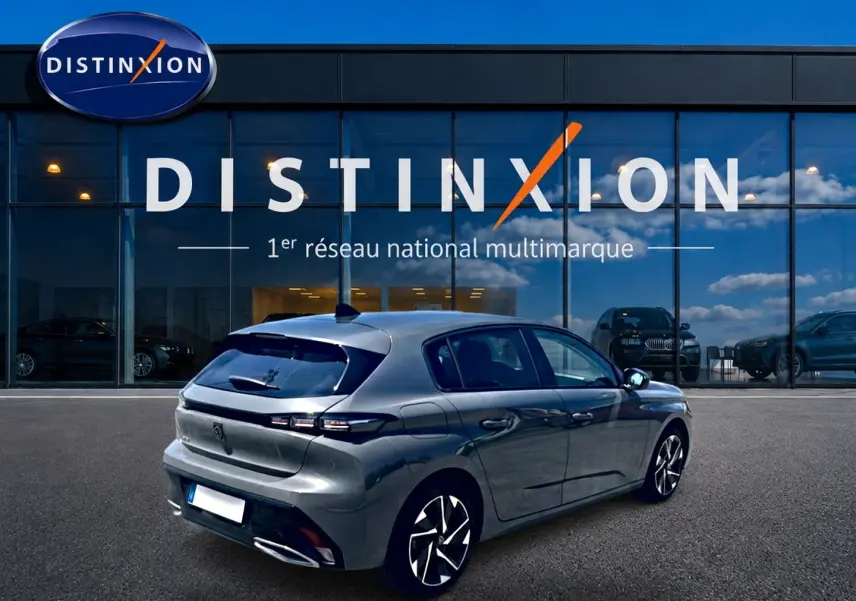 Vue 3/4 arrière droite d'une Peugeot 308 gris métallisé garée devant une vitrine avec logo Distinxion.