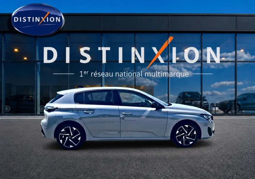 Profil droit d'une Peugeot 308 gris métallisé garée devant une vitrine avec logo Distinxion.