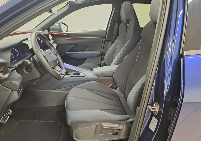 Vue intérieure côté conducteur du CUPRA TERRAMAR bleu cosmos, sièges sport noirs et éclairage d'ambiance orange sur la planche de bord.