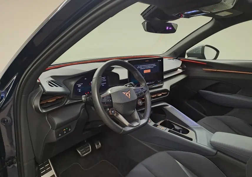 Vue intérieure côté conducteur du CUPRA TERRAMAR bleu cosmos, avec tableau de bord numérique et éclairage d'ambiance rouge.