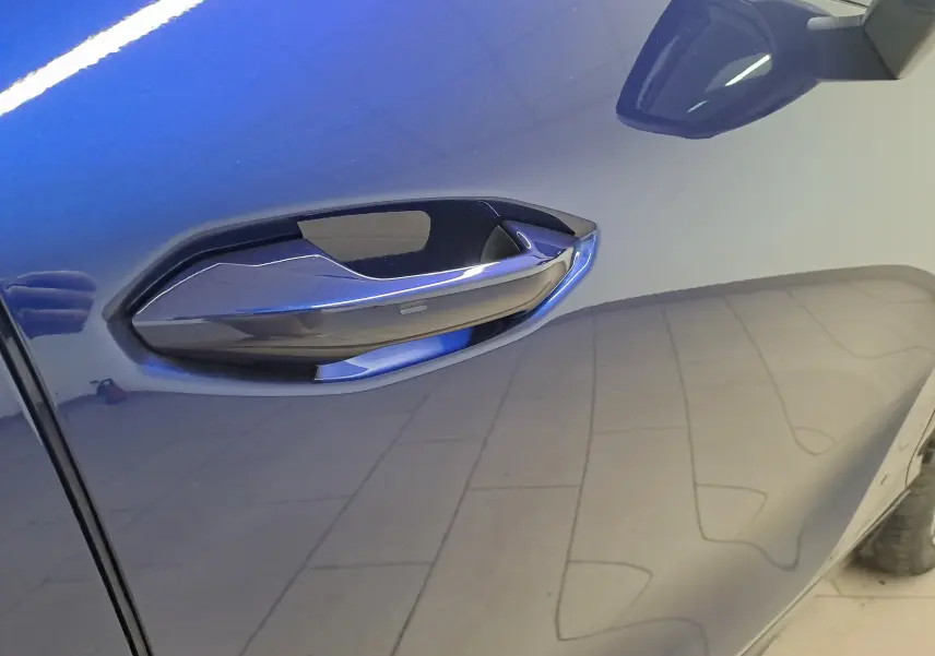 Poignée de porte côté gauche en gros plan sur CUPRA TERRAMAR bleu cosmos avec reflet du sol carrelé.