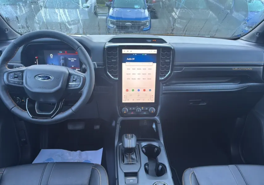 Vue intérieure avant du Ford Ranger Wildtrak 2026, tableau de bord noir avec écran tactile vertical et volant multifonctions.