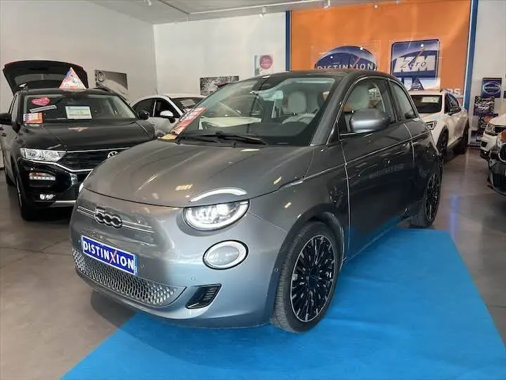 Fiat 500 électrique gris minéral métal vue 3/4 avant droit en showroom avec jantes noires distinctives.