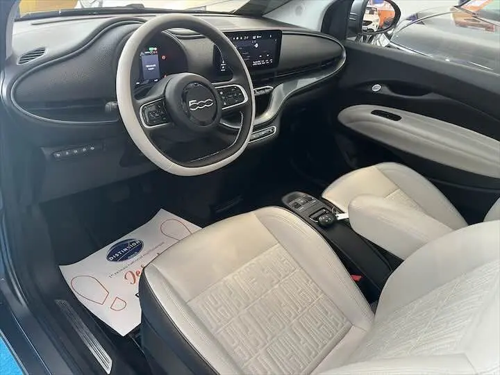 Intérieur avant droit de la Fiat 500 électrique gris minéral, sièges cuir clair et tableau de bord moderne avec écran tactile.
