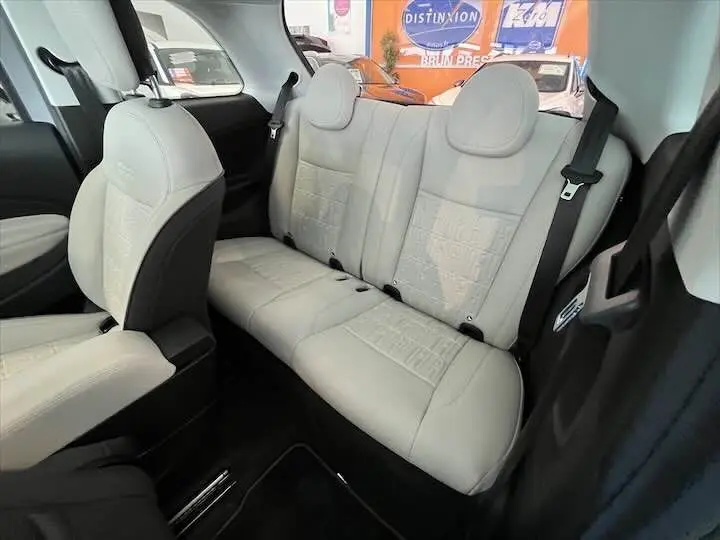 Intérieur arrière de la Fiat 500 électrique gris minéral métal, sièges en cuir clair avec motifs embossés visibles.
