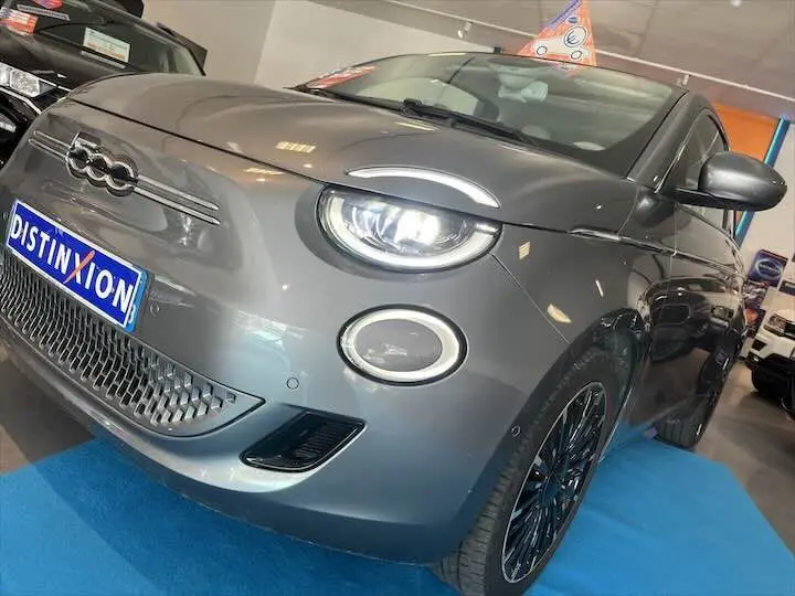 Vue 3/4 avant droit d'une FIAT 500 électrique gris minéral métal avec phares LED et jantes noires stylées.