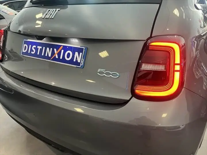 Vue arrière droite d'une FIAT 500 gris minéral métal avec feu arrière allumé et plaque Distinxion.