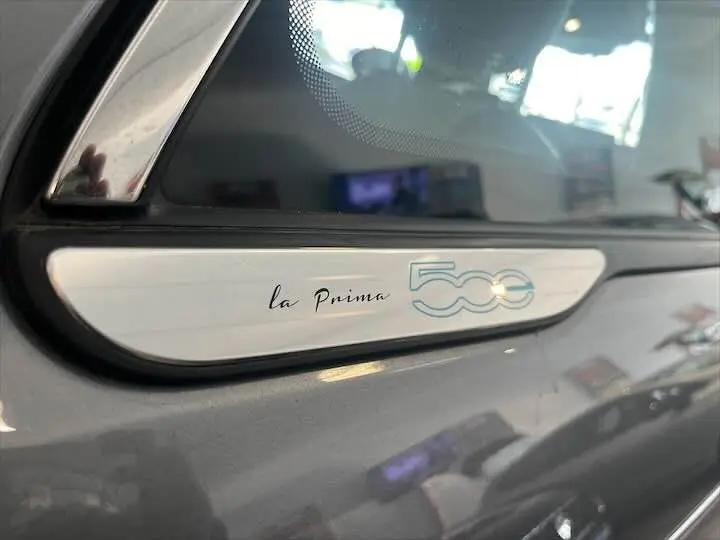 Gros plan sur l’inscription "la Prima 500" sur la portière gris minéral métal d’une Fiat 500 électrique.
