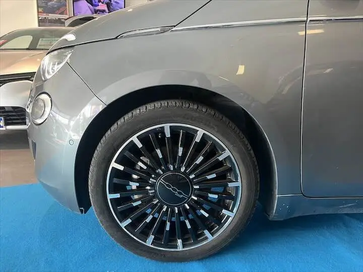 Gros plan sur la roue avant gauche et l'aile d'une Fiat 500 électrique gris minéral métal en intérieur showroom.