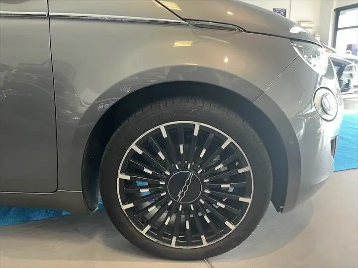 Gros plan sur la roue avant gauche d'une FIAT 500 électrique gris minéral métal, avec jante noire et argentée stylisée.