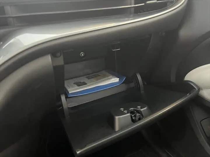 Gros plan sur la boîte à gants ouverte du Fiat 500 électrique gris minéral, montrant des documents à l'intérieur.