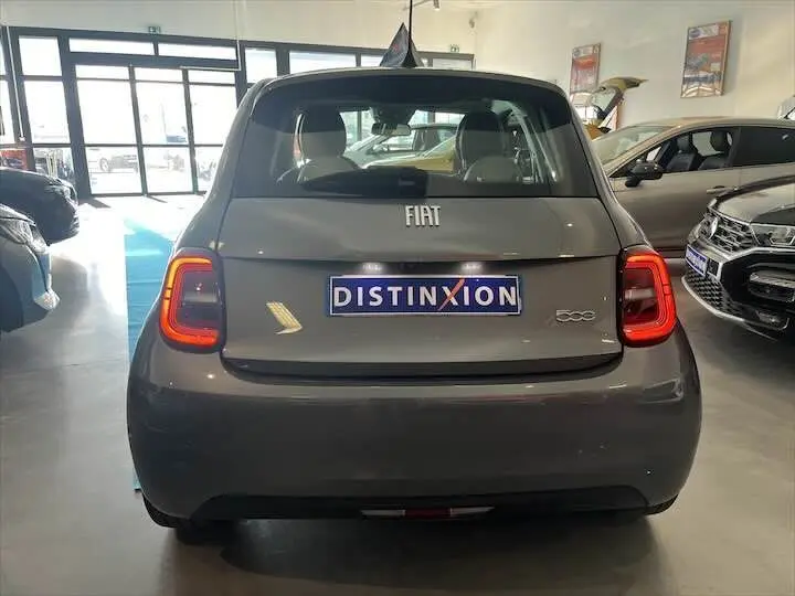 Vue arrière d'une Fiat 500 électrique gris minéral métal dans un showroom avec plaques Distinxion visibles